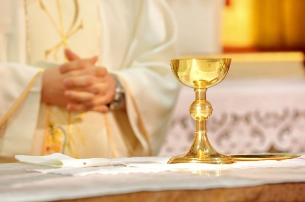 A photograph of a priest behind a golden cup.